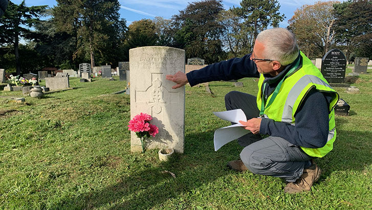 Middle aged man in hi-vis jacket inspects a CWGC headstone.