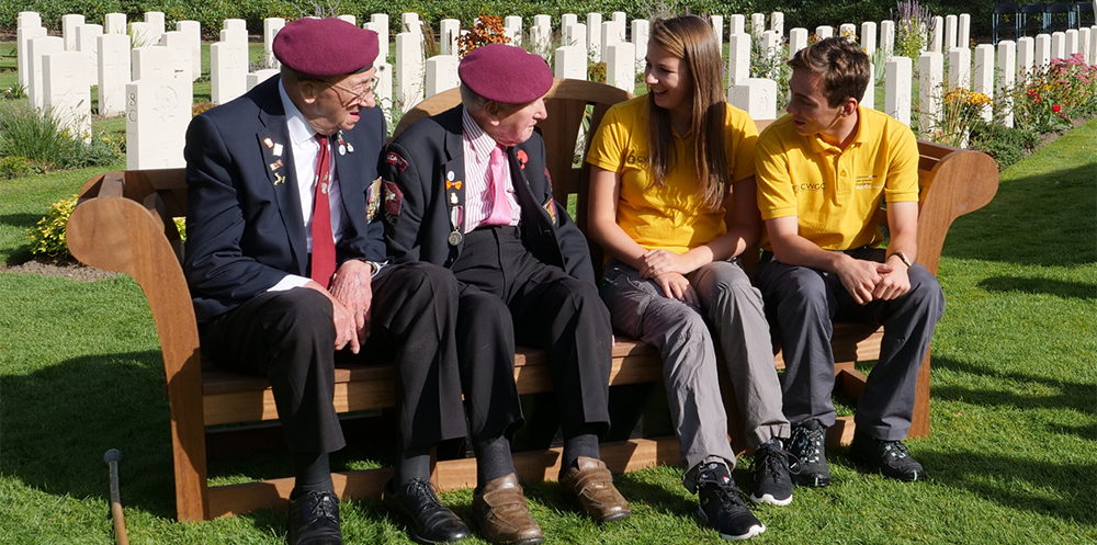 Arnhem veterans speak with CWGF Guides on a bench in a CWGC cemetery