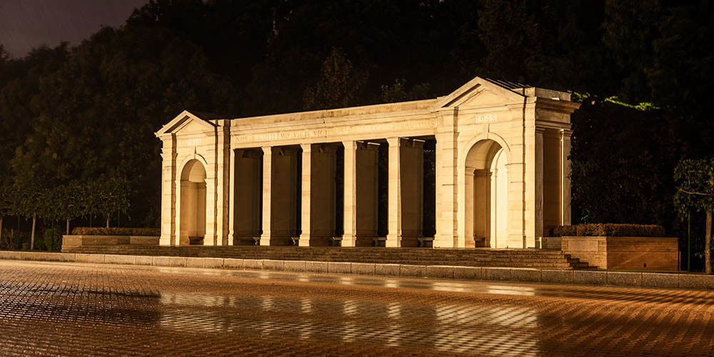 Bayeux Memorial at night. It has been raining, leaving a wet sheen on the stonework and patio in front of the memorial.