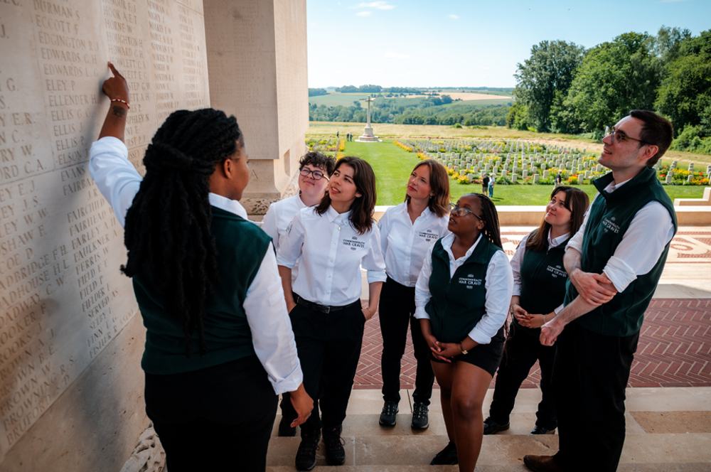 A CWGF Guide points to names on a name panel on the Thiepval Memorial in front of a group of fellow guides.